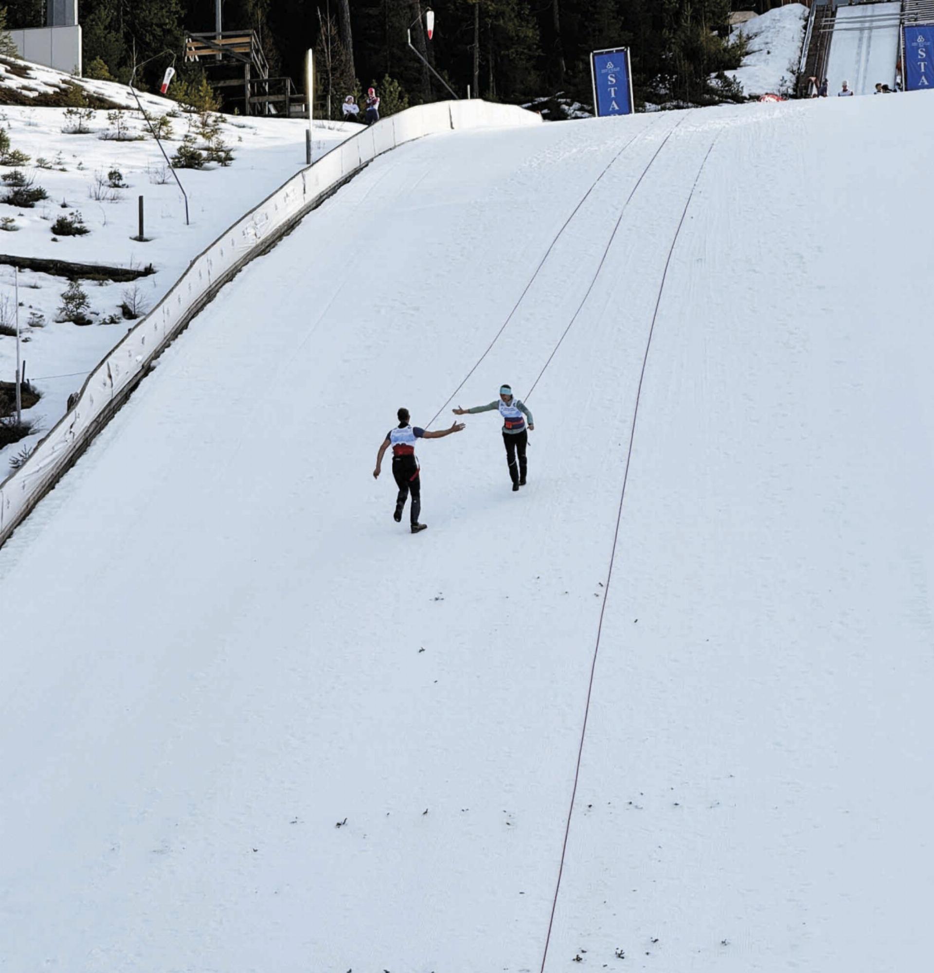 Über ein 120 Meter langes Seil verbunden, sprintet eine Person den Hang hinunter, während die andere gleichzeitig den Aufsprunghang hin auf läuft. Foto: o.K. - Das Bild wird blockiert. – Möglicherweise durch einen aktiven Adblocker.